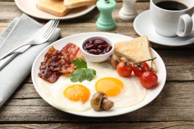 Geleneksel İngiliz kahvaltısı. Lezzetli, güneşli tarafı domuz pastırmalı, kırmızı fasulyeli, domatesli, mantarlı ve ahşap masada servis edilen kızarmış ekmekli yumurtalar.