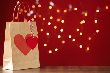 Tahta masada, kırmızı arka planda, üzerinde kalp izi olan, bulanık ışıklarla dolu bir kese kağıdı. Metin için boşluk