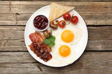 Geleneksel İngiliz kahvaltısı. Lezzetli, güneşli tarafı domuz pastırmalı, kırmızı fasulyeli, domatesli, mantarlı ve ahşap masadaki kızarmış ekmekli yumurtalar.