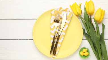 Paskalya kutlaması. Çatal bıçak takımı, çiçekler ve beyaz ahşap masaya boyanmış yumurtalar, düz yatak. Metin için boşluk