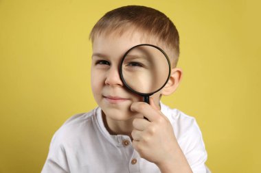 Sarı arka planda büyüteç olan küçük çocuk.