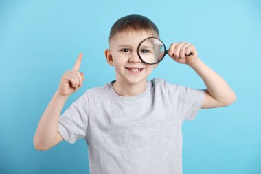 Açık mavi arka planda büyüteç takan küçük çocuk.