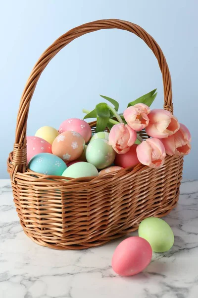 Boyanmış Paskalya yumurtaları ve hasır sepetteki güzel laleler beyaz mermer masada, yakın plan.