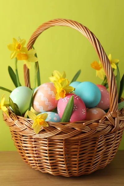 Boyanmış Paskalya yumurtaları ve ahşap sepetin içindeki nergisler açık yeşil arka planda, yakın planda.