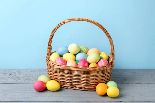 Hasır sepetin içine boyanmış Paskalya yumurtaları açık mavi arka plana karşı gri ahşap masa üzerinde