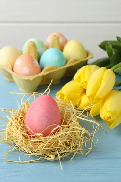 Kutuda boyanmış Paskalya yumurtaları, yuva ve açık mavi ahşap masa üzerinde güzel laleler, yakın plan.