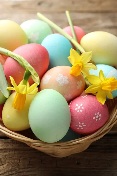 Boyanmış Paskalya yumurtaları ve ahşap masadaki hasır sepetin içindeki güzel nergisler.