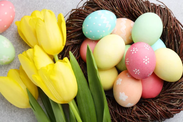 Yuvada boyanmış Paskalya yumurtaları ve gri masada güzel laleler.