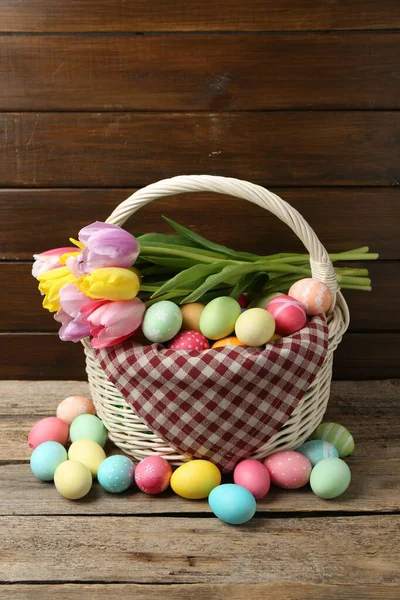 Hasır sepete boyanmış Paskalya yumurtaları ve ahşap masada güzel laleler.