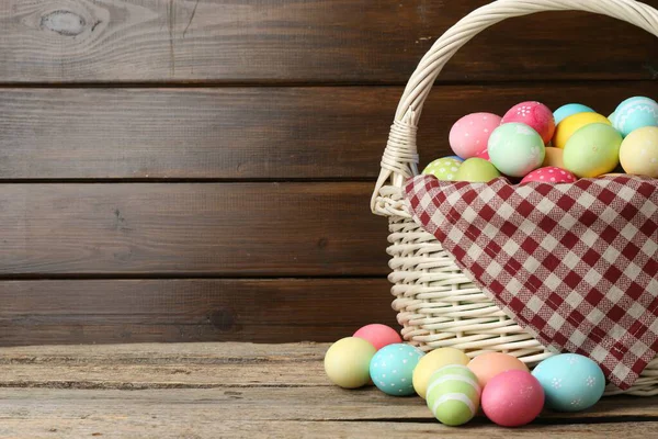 Tahta masadaki hasır sepete boyanmış Paskalya yumurtaları. Metin için boşluk