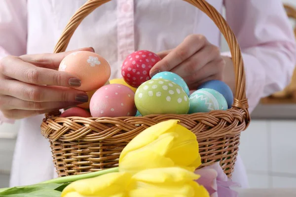Paskalya sepetinde yumurta boyalı bir kadın ve beyaz masa içinde laleler, yakın plan.