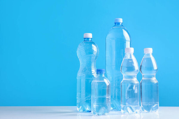 Water bottles of different sizes on white table against light blue background, space for text