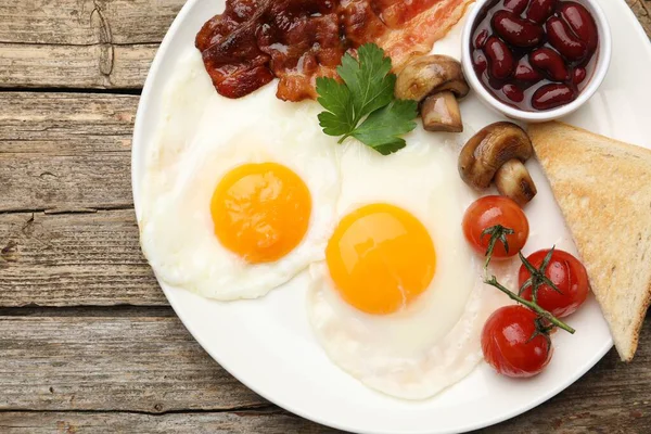 Geleneksel İngiliz kahvaltısı. Lezzetli, güneşli tarafı domuz pastırmalı, kırmızı fasulyeli, domatesli, mantarlı ve ahşap masadaki kızarmış ekmekli yumurtalar.