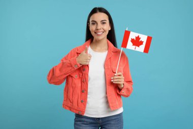 Kanada bayrağı taşıyan mutlu kadın açık mavi arka planda onay veriyor
