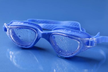 Mavi yüzeyde su damlaları olan yüzme gözlükleri, yakın plan.