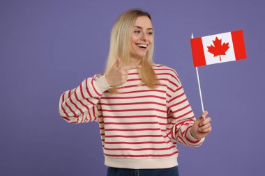 Mutlu kadın elinde pastel mor arka planda Kanada bayrağını gösteriyor.