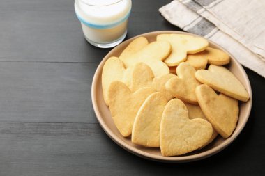 Lezzetli kalp şeklinde tereyağlı kurabiye ve süt koyu ahşap masada, yakın plan. Metin için boşluk
