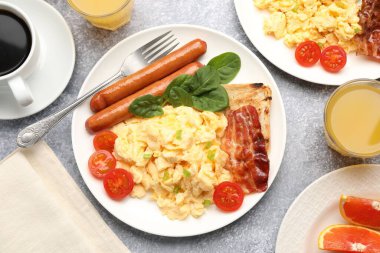 Lezzetli bir kahvaltı. Lezzetli çırpılmış yumurta, domuz pastırması, sosis ve domatesler gri dokuma masasında servis ediliyor.