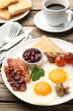 Geleneksel İngiliz kahvaltısı. Lezzetli, güneşli tarafı domuz pastırmalı, kırmızı fasulyeli, domatesli, mantarlı ve ahşap masada servis edilen kızarmış ekmekli yumurtalar.