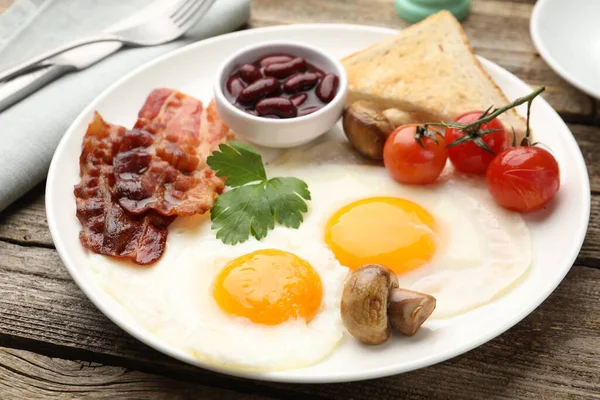 Geleneksel İngiliz kahvaltısı. Lezzetli, güneşli tarafı domuz pastırmalı, kırmızı fasulyeli, domatesli, mantarlı ve ahşap masada servis edilen kızarmış ekmekli yumurtalar.