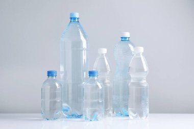 Beyaz masada gri arka planda farklı boyutlarda su şişeleri