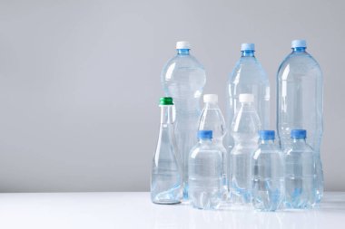 Beyaz masada gri arkaplan ile farklı boyutlarda su şişeleri, metin için boşluk