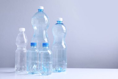 Beyaz masada gri arkaplan ile farklı boyutlarda su şişeleri, metin için boşluk