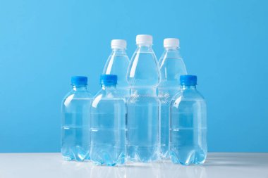 Açık mavi arka planda beyaz masada farklı boyutlarda su şişeleri