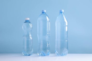 Açık mavi arka planda beyaz masada farklı boyutlarda su şişeleri