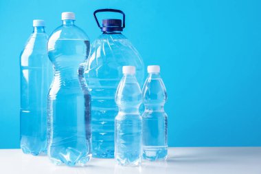 Beyaz masada farklı boyutlarda su şişeleri açık mavi arkaplan, metin için boşluk