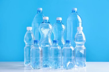 Açık mavi arka planda beyaz masada farklı boyutlarda su şişeleri