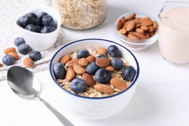 Yulaf gevreği, badem sütü, yaban mersini ve fındık beyaz ahşap masada, yakın plan.