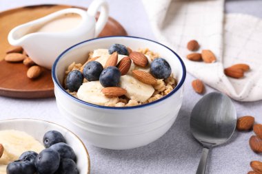 Bademli yulaf gevreği, yaban mersini, muz ve süt açık gri masada, yakın plan.