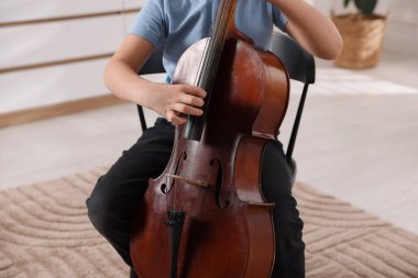 Evdeki sandalyede keman çalan küçük çocuk, yakın plan.