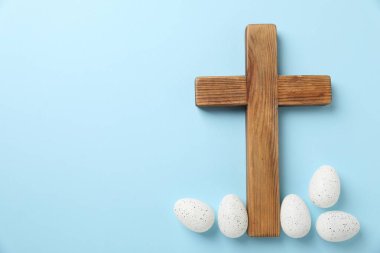 Ahşap haç ve paskalya yumurtaları açık mavi arka planda, düz yerde. Metin için boşluk