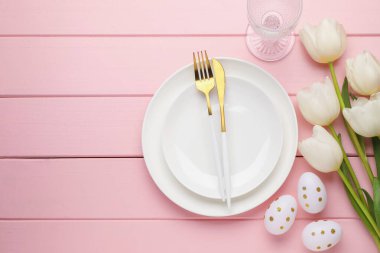 Paskalya kutlaması. Çiçeklerle, çatal bıçaklarla ve pembe ahşap masaya boyanmış yumurtalarla süslü bir ortam. Metin için boşluk