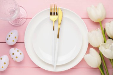 Paskalya kutlaması. Çiçeklerle, çatal bıçaklarla ve pembe ahşap masaya boyanmış yumurtalarla süslü bir ortam.