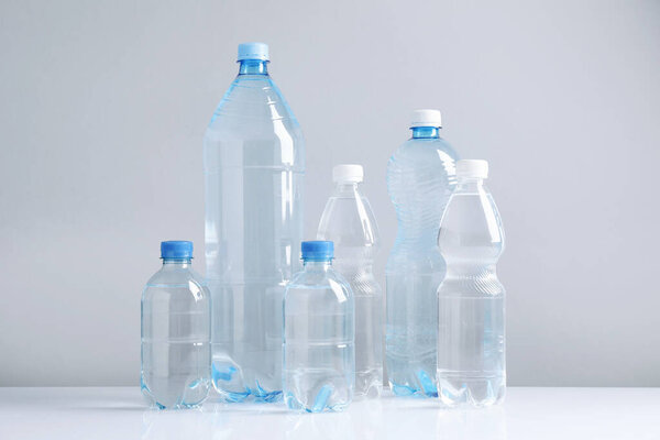 Water bottles of different sizes on white table against grey background