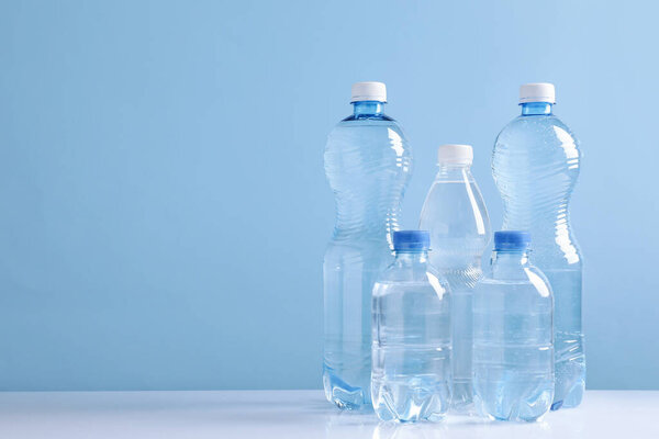 Water bottles of different sizes on white table against light blue background. Space for text