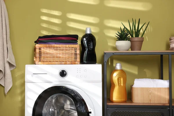 Çamaşır sepetinin içinde çamaşır makinesinin üzerinde katlanmış temiz kıyafetler var.