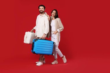 Kırmızı arka planda bavulları olan mutlu çift, mesaj için boşluk