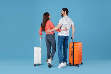 Açık mavi arka planda bavulları olan mutlu bir çift.