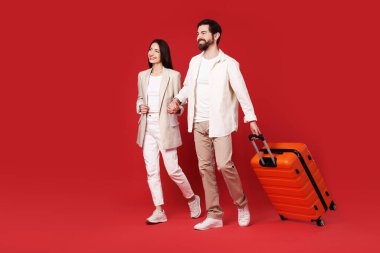 Kırmızı arka planda bavulu olan mutlu çift.