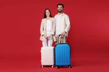 Kırmızı arka planda bavulları olan mutlu çift.