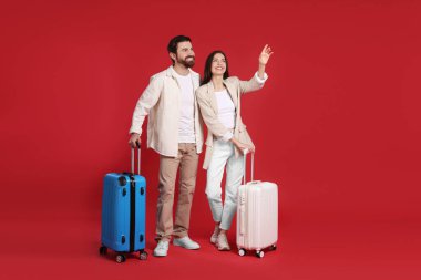 Kırmızı arka planda bavulları olan mutlu çift, mesaj için boşluk