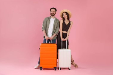 Pembe arka planda bavulları olan mutlu çift.