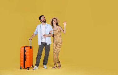 Sarı arka planda bavulu olan mutlu çift, mesaj için boşluk