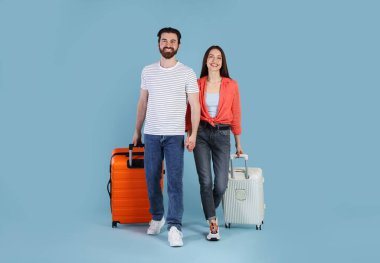 Açık mavi arka planda bavulları olan mutlu çift.