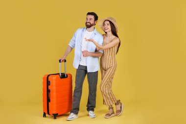 Sarı arka planda bavulu olan mutlu çift.