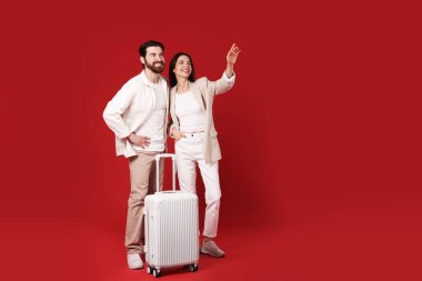 Kırmızı arka planda bavulu olan mutlu çift, mesaj için boşluk
